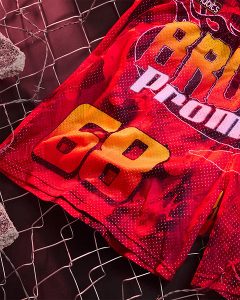 Red active short with yellow and pink graphic design and perforated mesh panels, displayed flat on geometric background.