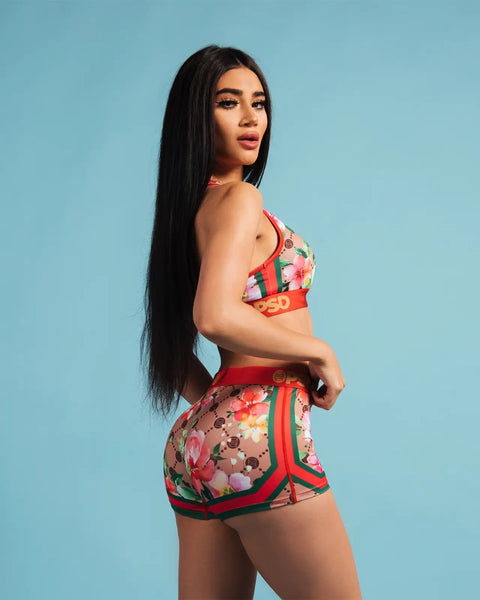 Woman wearing floral print bikini set with red trim and colorful flower pattern against blue background.