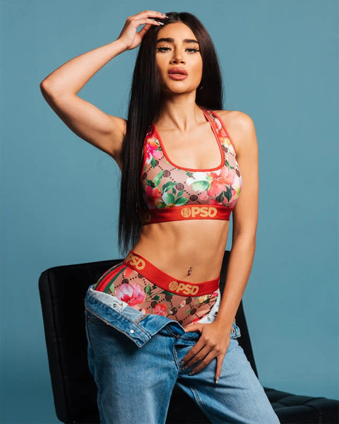 Woman wearing red sports bra and matching shorts with multicolored floral print and red elastic waistbands against blue backg
