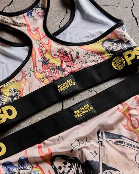 Sports bra with colorful graphic print featuring red flames, skulls, and illustrated figures on cream fabric with black strap