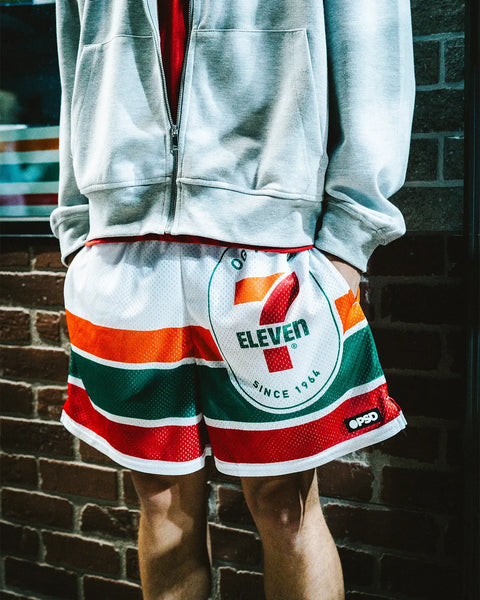 7-Eleven athletic shorts with red, green, and white horizontal stripes and logo on front, worn with gray zip-up jacket.