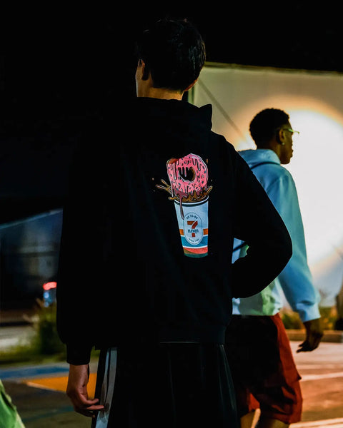 Black hoodie with pink frosted donut and 7-Eleven cup graphic printed on back.