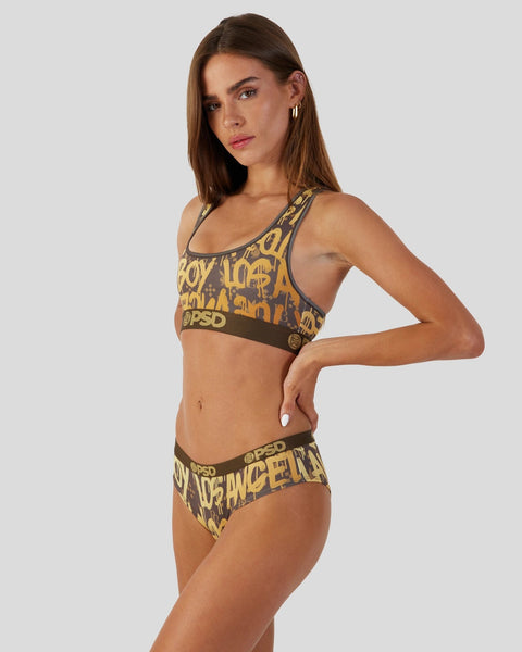 Woman wearing gold and brown Playboy graffiti-print sports bra and matching briefs with elastic waistband.